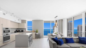 A modern kitchen with stainless steel appliances, a central island with bar stools, and a dining area with a view of the ocean. - Wrap Around Balcony + Pool + Steps to the Beach (Hollywood)
