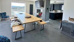 A spacious living area with a long wooden table, benches, and a kitchen area with dark cabinets and a TV. - Luxury 5 Bed - Sleeps 14 - With Swimming Pool (Bristol)