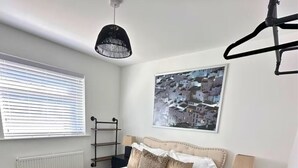 A bedroom with a bed, a radiator, a window with blinds, a hanging light fixture, a nightstand, and a wall-mounted shelf. - Luxury 5 Bed - Sleeps 14 - With Swimming Pool (Bristol)