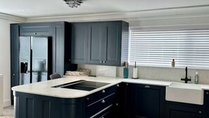 A modern kitchen with dark cabinetry, a central island, and a built-in sink. - Luxury 5 Bed - Sleeps 14 - With Swimming Pool (Bristol)