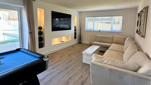 Un salon comprenant une table de billard, un canapé, une table basse et un téléviseur fixé au mur.