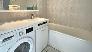 Un baño pequeño con lavadora, lavamanos y bañera.