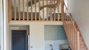 Une pièce de style loft comprenant un coin cuisine, une table à manger avec des chaises et un escalier en bois.