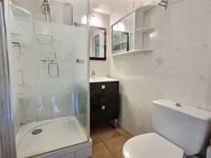 Et badeværelse med glasbrusekabine, en hvid vask, et sort skab og et hvidt toilet.