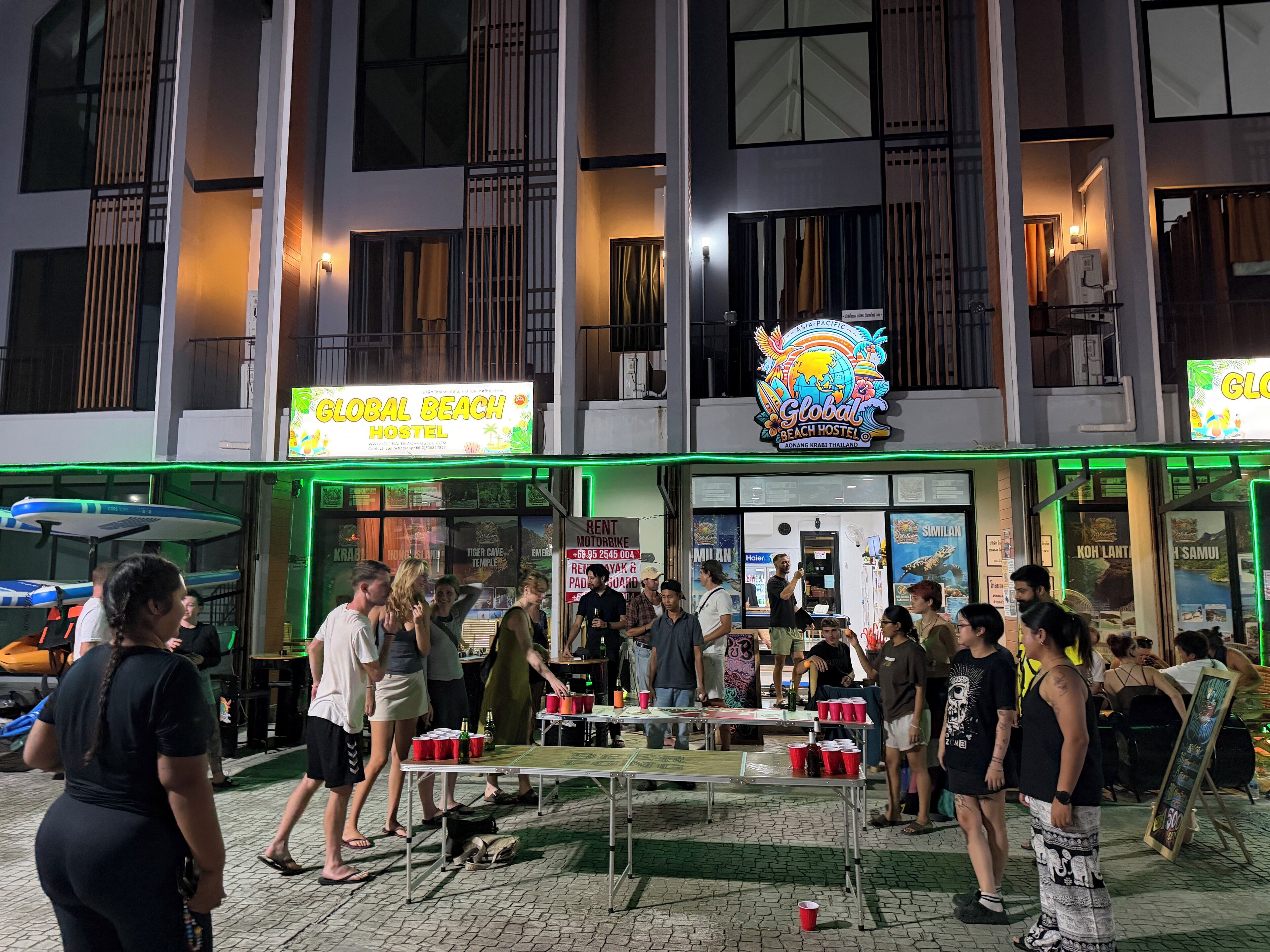 Et hostel med stort skilt, udendørs siddeområde og en poolbar.