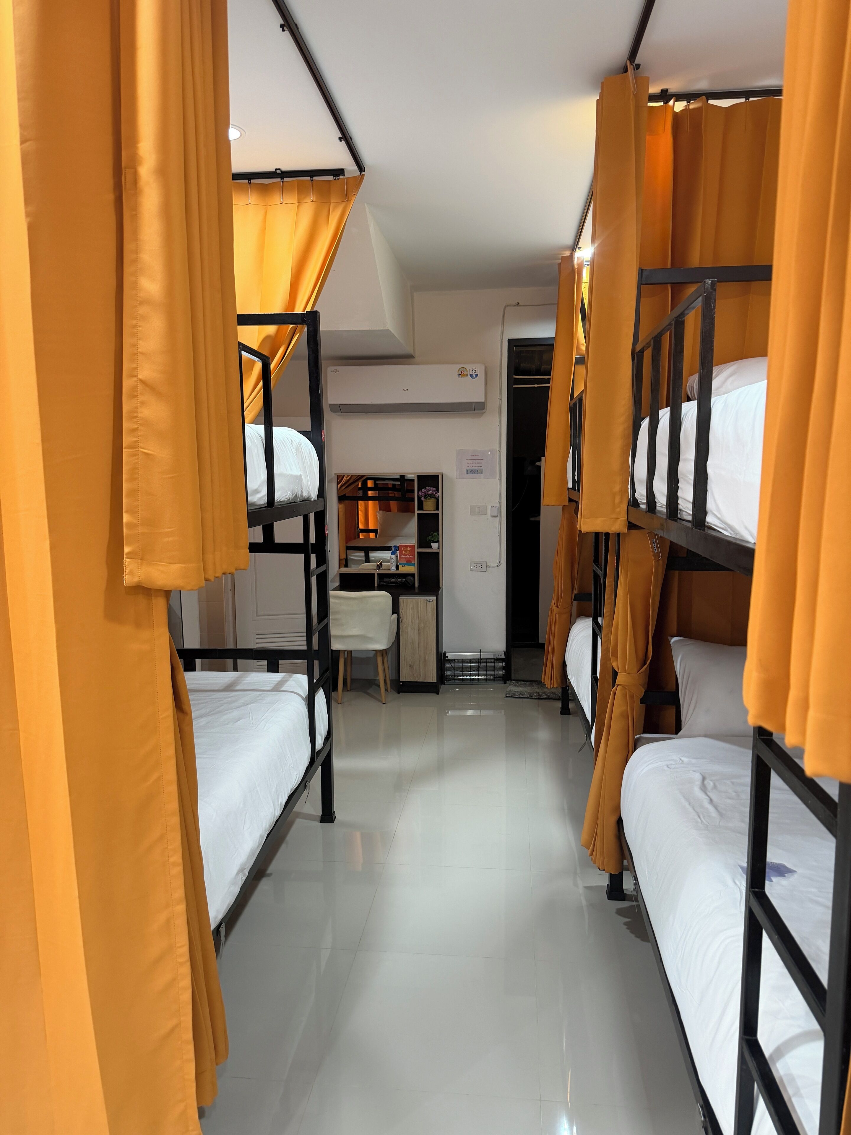 A dormitory room with bunk beds, a desk, a chair, and an air conditioning unit.