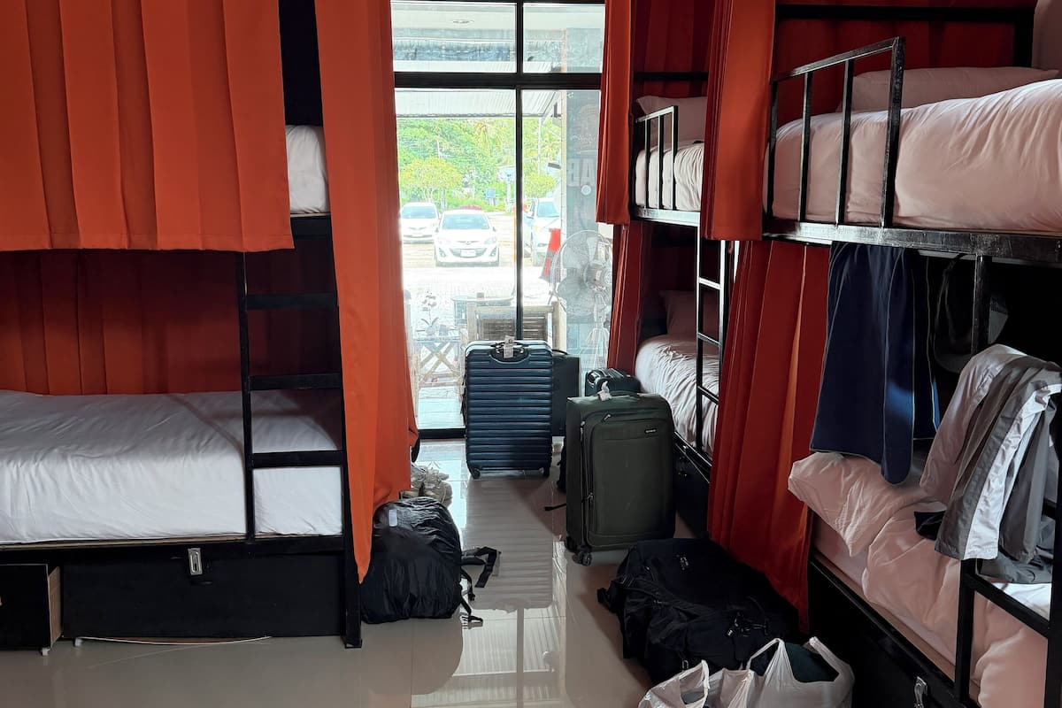 Une chambre de type dortoir, avec des lits superposés, une grande fenêtre et un ventilateur.