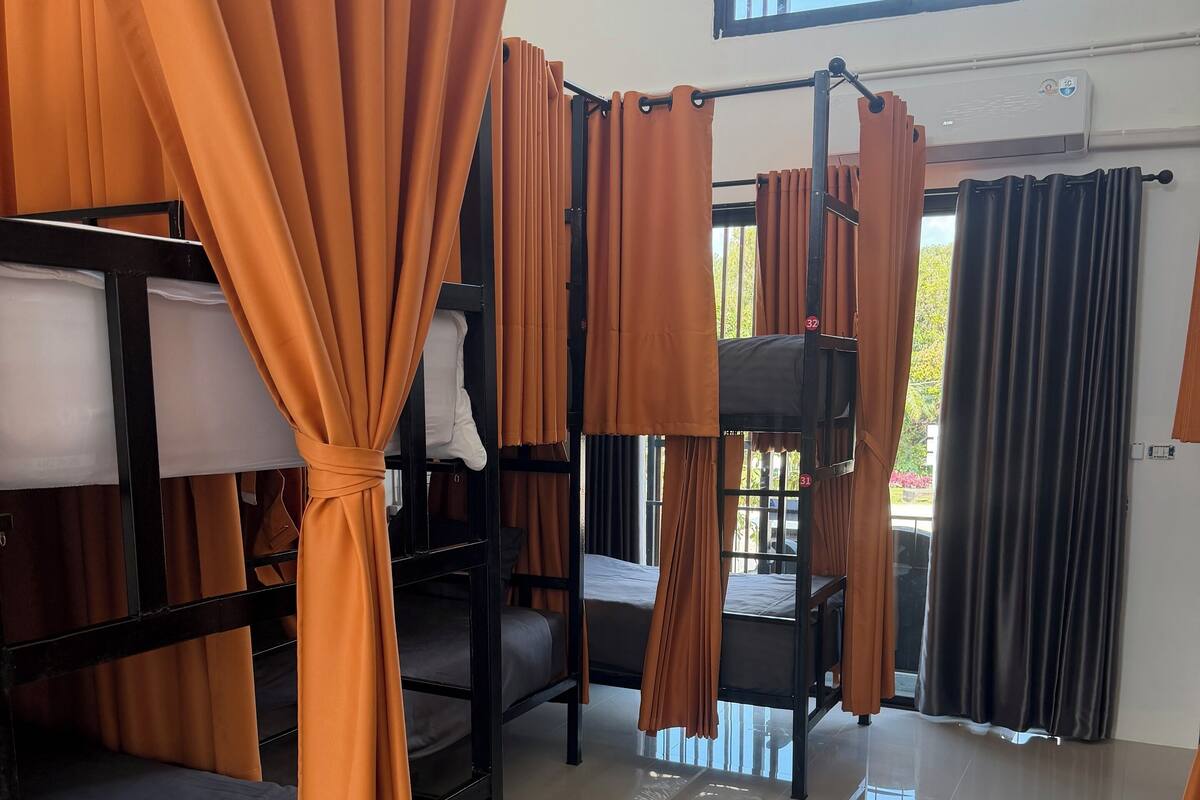 Une chambre de dortoir avec des lits superposés, des rideaux orange et une fenêtre donnant sur un paysage verdoyant.