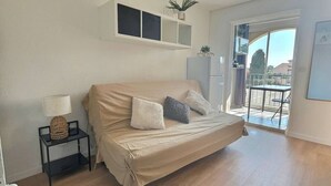 Een slaapkamer met een bed, een klein nachtkastje met een lamp, een plank met decoratieve objecten en een uitzicht op het balkon.