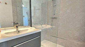Een moderne badkamer met een douchecabine van glas, een grote spiegel en een wastafelmeubel met een wastafel en lades.