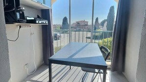 Een balkon met een tafel, stoelen, een koffiezetapparaat en een televisie op een plank.