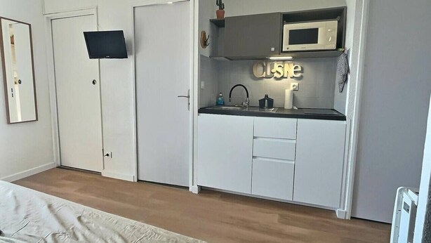 Een kleine keuken met witte kasten, een magnetron en een spoelbak.