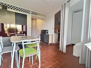 A compact kitchen with white appliances, a dining area with a table and chairs, and a tiled floor. - T2 en Rez de jardin plage de Miramar (La Londe-les-Maures)