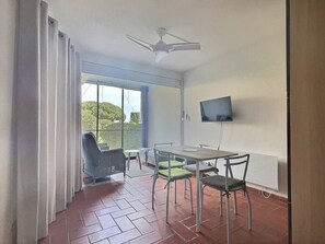 A balcony with a table and chairs, a ceiling fan, and a TV mounted on the wall. - T2 en Rez de jardin plage de Miramar (La Londe-les-Maures)