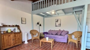 Un soggiorno con un divano viola, due poltrone in vimini, un tavolino in legno e un mobiletto in legno.