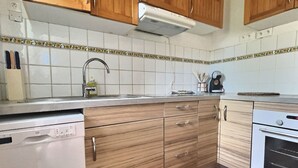 A kitchen with wooden cabinets, a dishwasher, a stove, and a tiled backsplash. - Joli Mazet T3 avec piscine (La Londe-les-Maures)