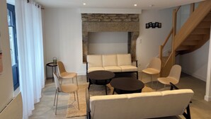 Un salon moderne avec une cheminée en pierre, un canapé, deux fauteuils, une table basse et un escalier.