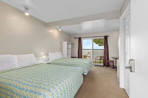 A hotel room with two beds, a small table, a chair, and a view of the outdoors.