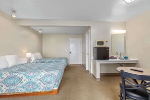Camera d'albergo compatta con un letto, una scrivania con un forno a microonde, una sedia e un tavolino.