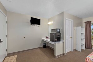 A hotel room with a kitchenette, a flat-screen TV mounted on the wall, a door leading to a balcony, and a bed with a colorful bedspread. - Upper Level Lakeview Room (Lake City)