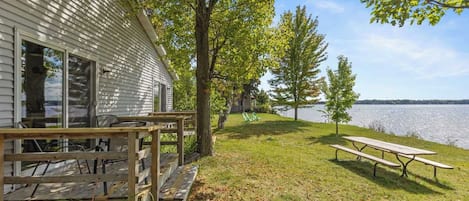 Una cabaña junto al lago con terraza de madera y mesa de picnic.
