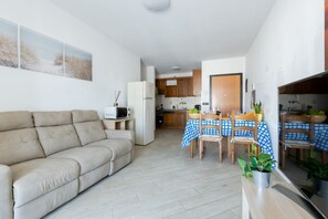 Una sala de estar con sofá, una mesa de comedor con sillas, una zona de cocina y un televisor.