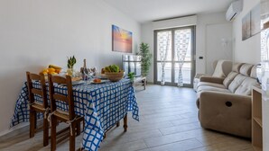 A dining area with a table set for two, a sofa, and a window with curtains. - GuestHost - Cozy 86 sqm apartment, able to comfortably accommodate up to 4 people, located on the third floor of a building with lift.The property, located in a quiet residential area, is about 2 km from Piazza Vittorio Emanuele II and the center of Pisa (Pisa)