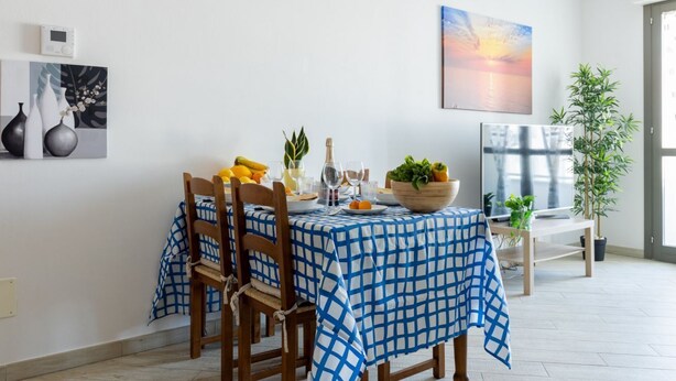 A dining area with a checkered tablecloth, wooden chairs, a bowl of fruit, a bottle, and a painting on the wall. - GuestHost - Cozy 86 sqm apartment, able to comfortably accommodate up to 4 people, located on the third floor of a building with lift.The property, located in a quiet residential area, is about 2 km from Piazza Vittorio Emanuele II and the center of Pisa (Pisa)