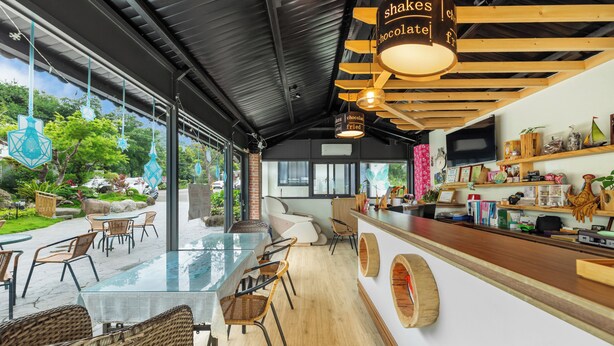Een modern café met een glazen eetgedeelte, rieten stoelen en een houten bar.