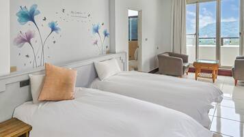 Une chambre d’hôtel avec deux lits, une petite table, une chaise et une grande fenêtre donnant sur l’extérieur.