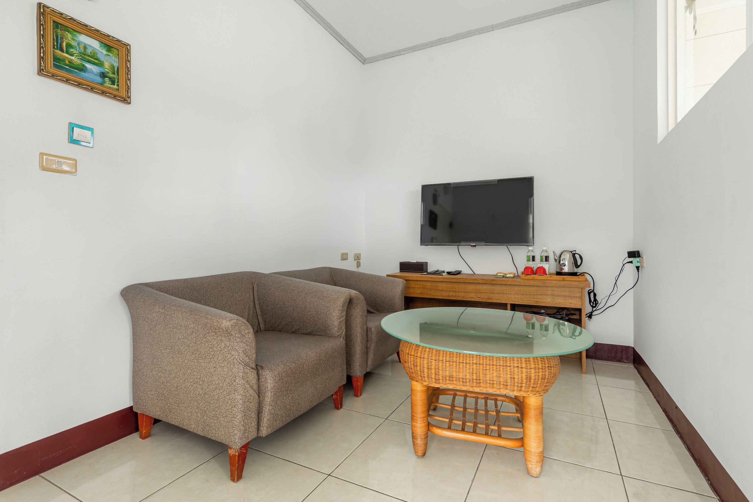 Uma sala de estar com sofá, mesa de vidro, TV fixada na parede e um armário de madeira.