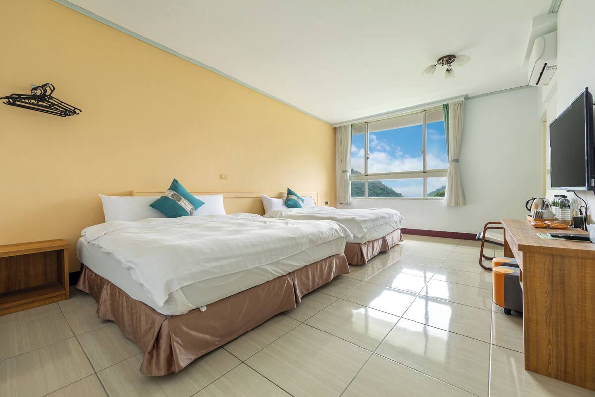 Une chambre d’hôtel avec deux lits, un bureau, une chaise, une télévision et une fenêtre donnant sur un beau paysage.