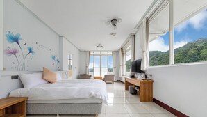 Een slaapkamer met een bed, een bureau, een televisie en een groot raam met uitzicht op een bos.