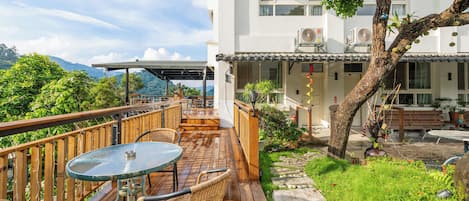 A wooden deck with a table and chairs, a stone pathway, and a building with a balcony.