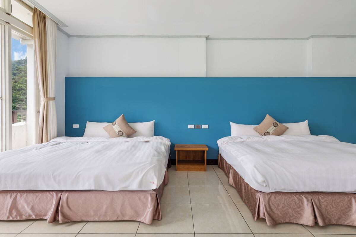 Une chambre d’hôtel avec deux lits, un mur d’accent bleu et une vue sur la verdure.