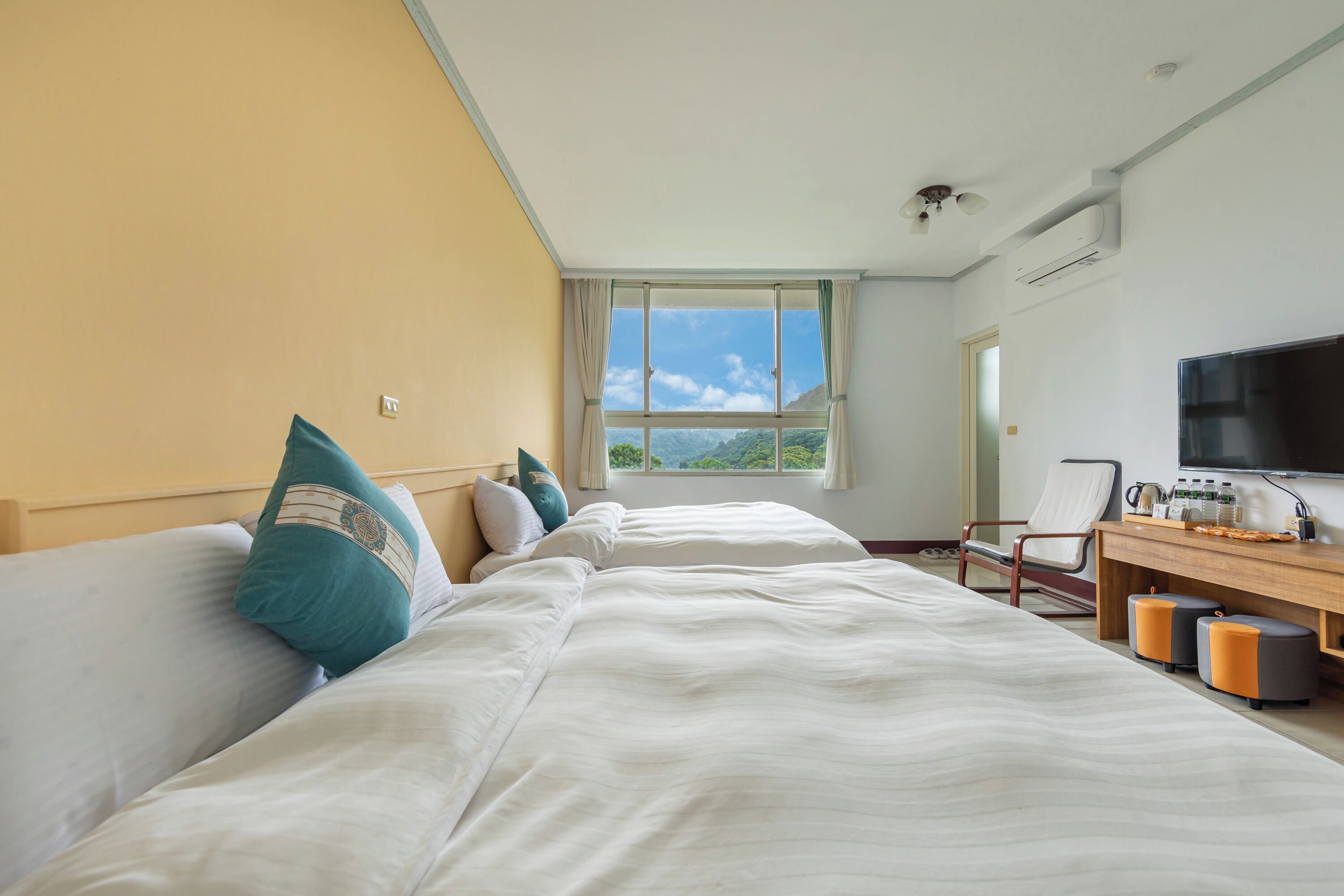 Ein Hotelzimmer mit zwei Betten, einem Schreibtisch mit Fernseher und Blick auf die Berge.