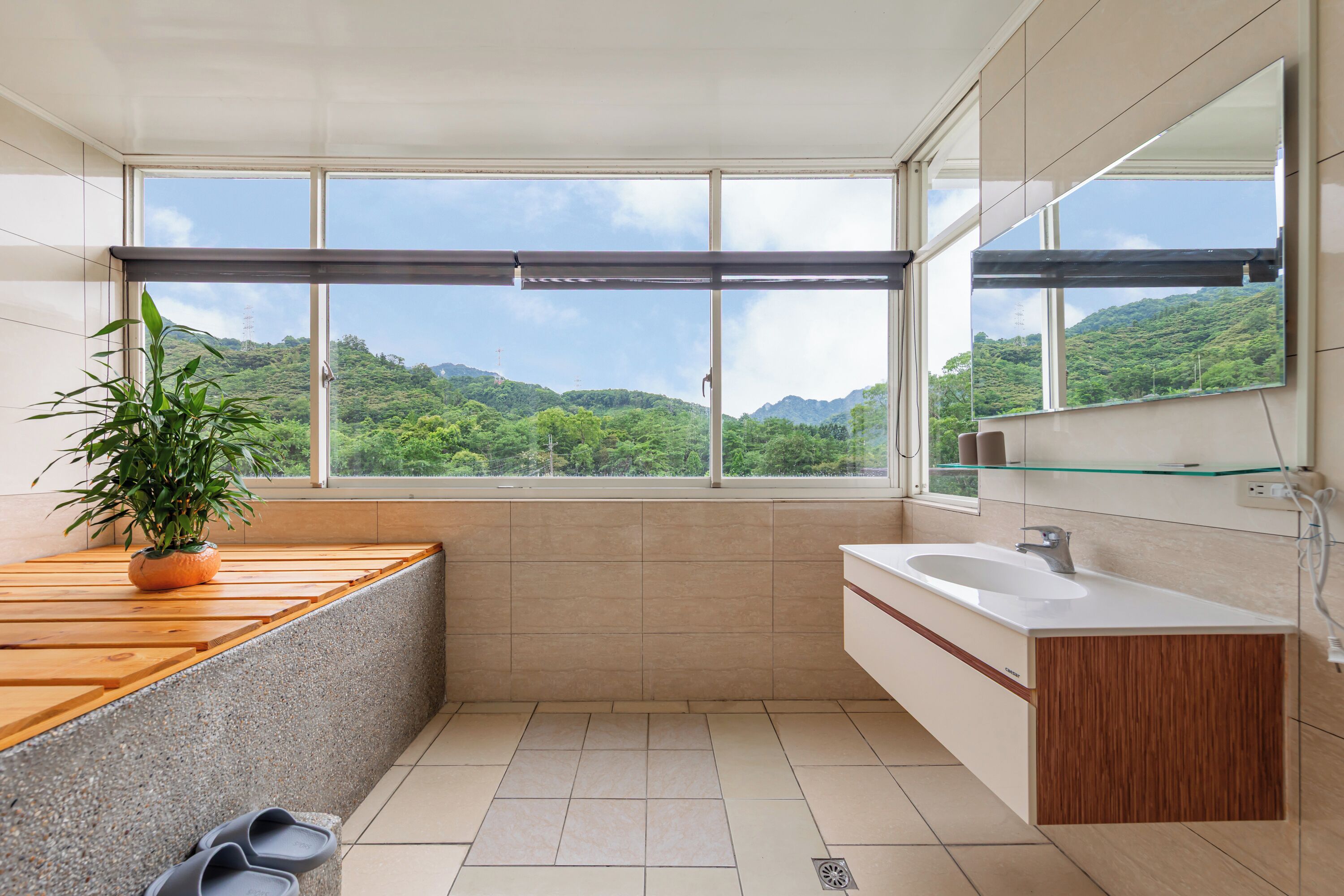 A modern bathroom with a large window, a wooden countertop, a sink, and a potted plant.