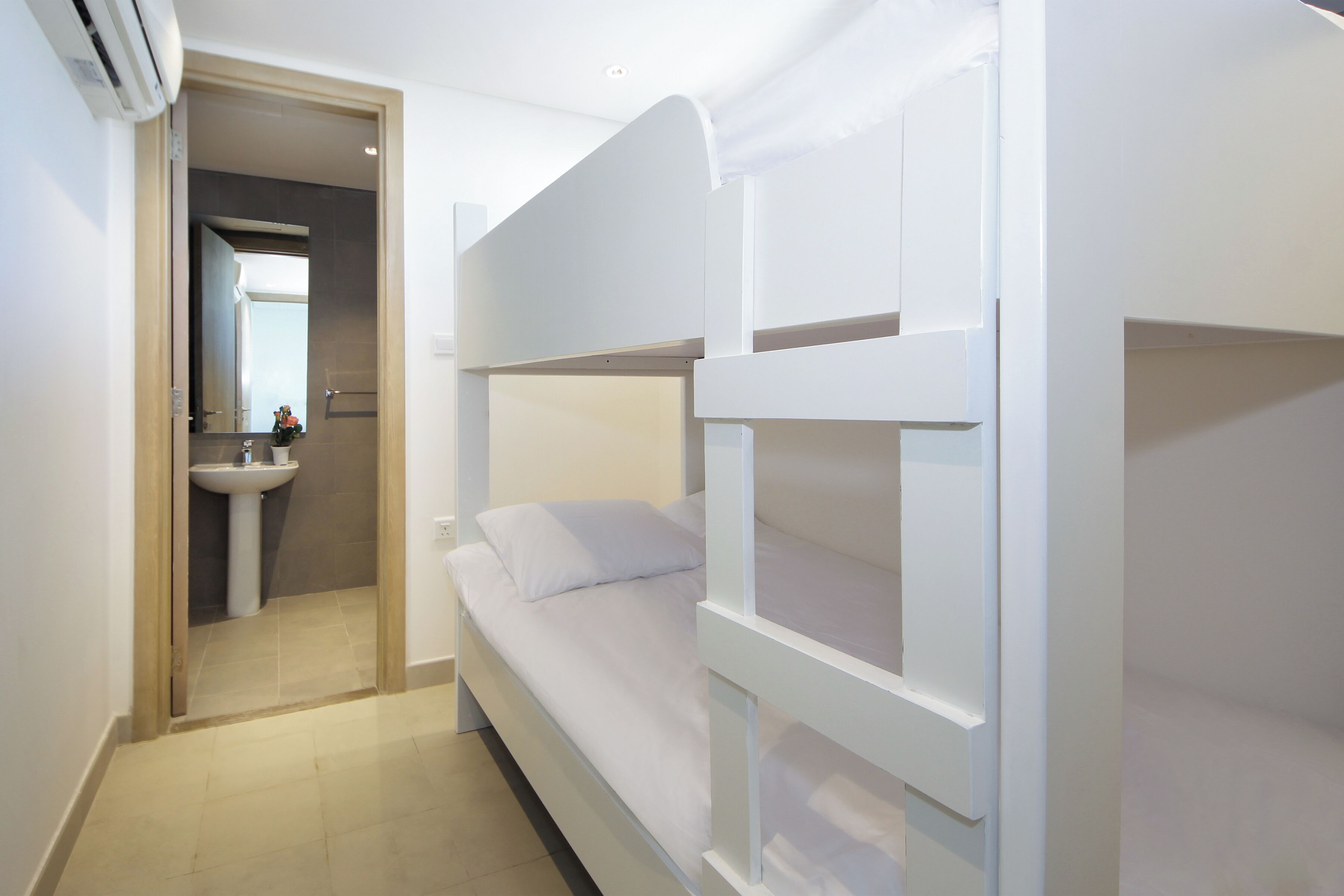 Habitación con literas y un baño contiguo con lavamanos y espejo.