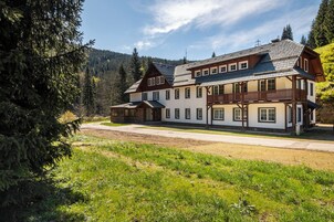 Un chalet grande de dos pisos con balcón, rodeado de bosque y cielo despejado.