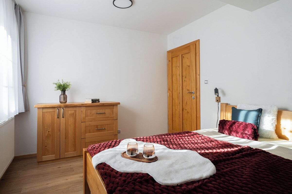 A bedroom with a wooden wardrobe, a bed with a red blanket, and a bedside table with two glasses.