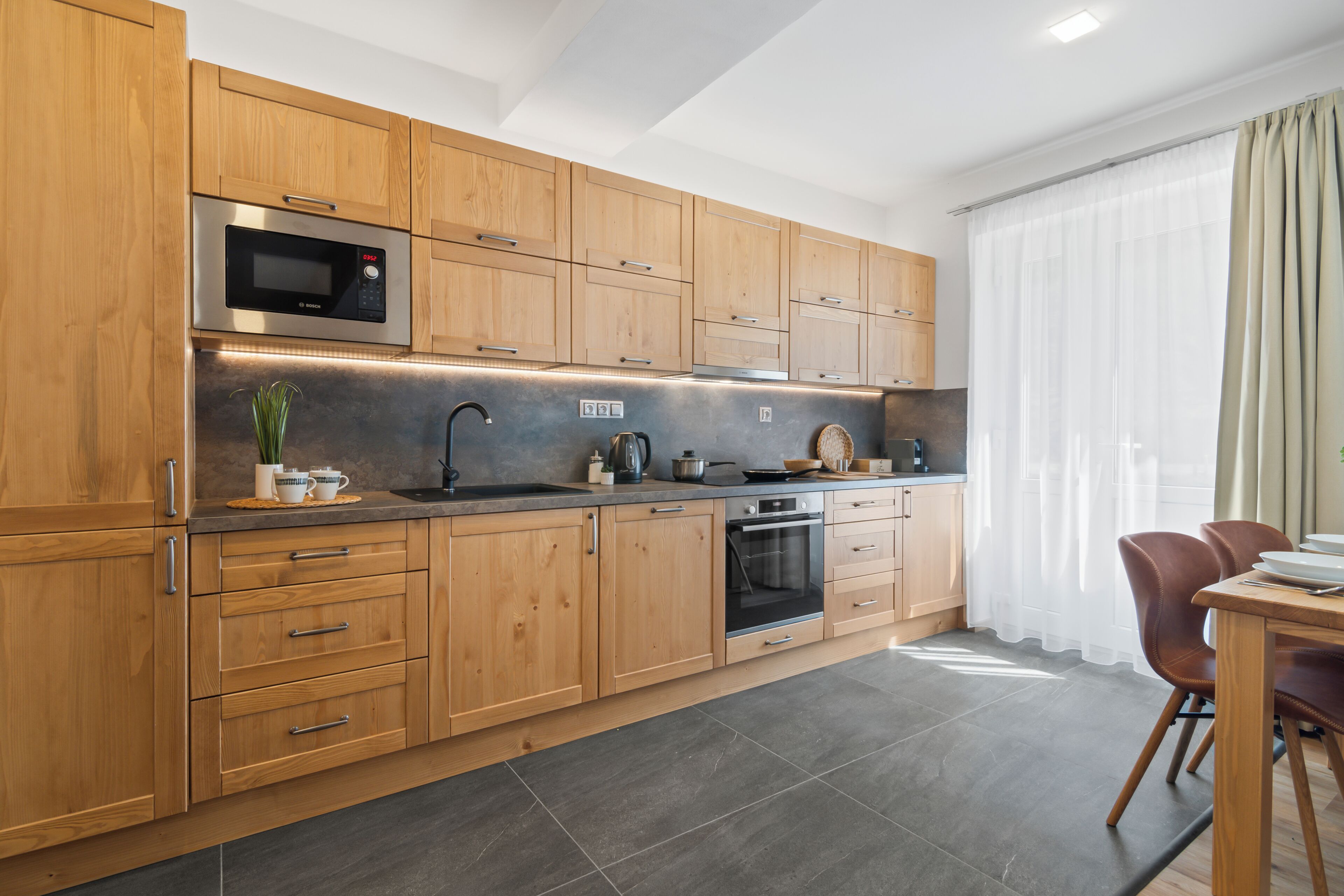 A modern kitchen with wooden cabinets, a microwave, oven, and a dining area with chairs.