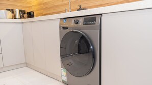 A modern kitchen with a built-in washer and dryer, white cabinetry, and a wooden countertop. - 118 4A/ Luxury ground floor studio apartment (Riyadh)
