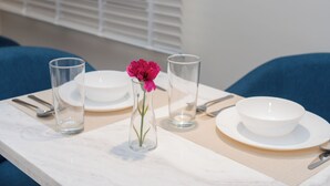 A dining table with a vase of pink flowers, clear glasses, and white plates and bowls. - 118 4A/ Luxury ground floor studio apartment (Riyadh)