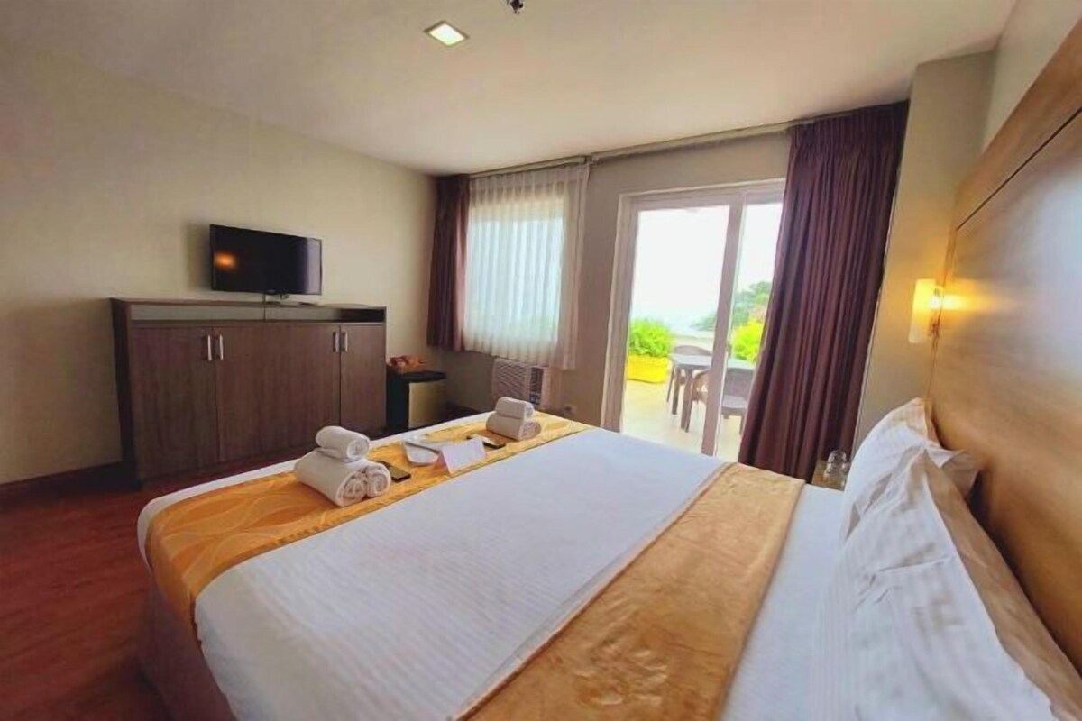 A hotel room with a bed, a television on a stand, a desk with a chair, and a view of the outdoors through a sliding door.