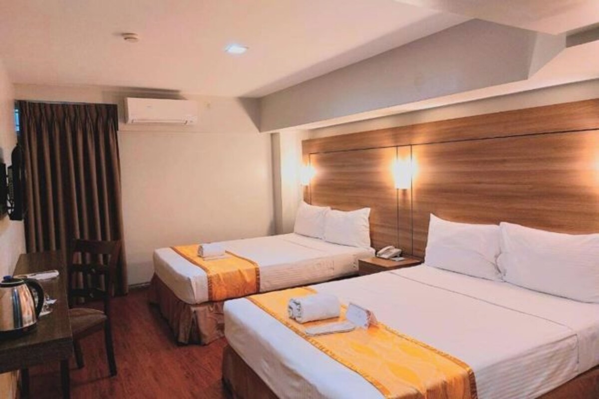 A hotel room with two beds, a wooden headboard, a desk with a kettle, and a chair.