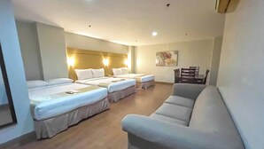 Een hotelkamer met twee eenpersoonsbedden, een slaapbank en een eettafel met stoelen.