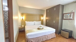 Een hotelkamer met een groot bed, een kledingkast, een nachtkastje met een lamp en een kleine koelkast.