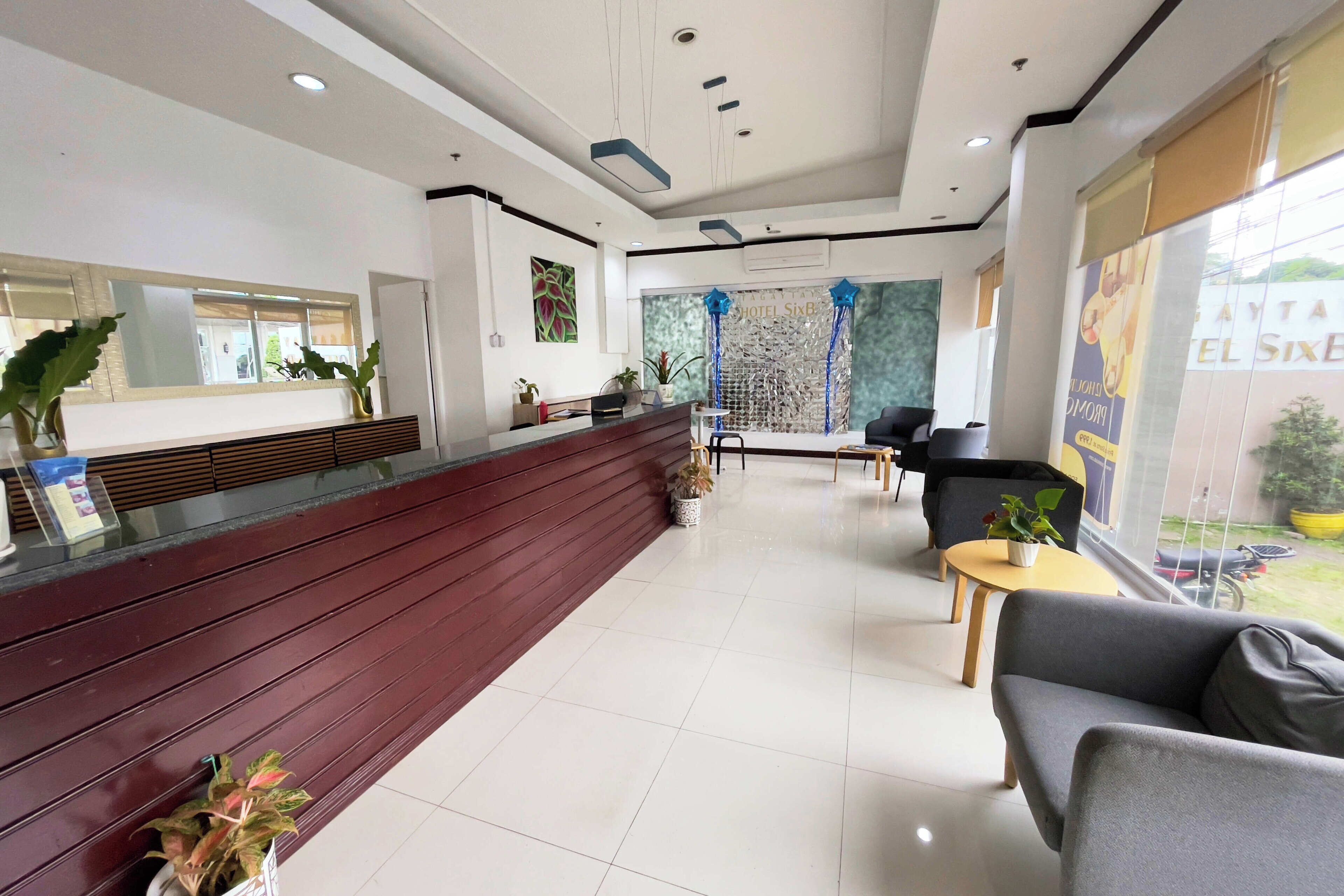 A hotel reception area with a wooden reception desk, a seating area with sofas and chairs, and a large window offering a view of the outside.