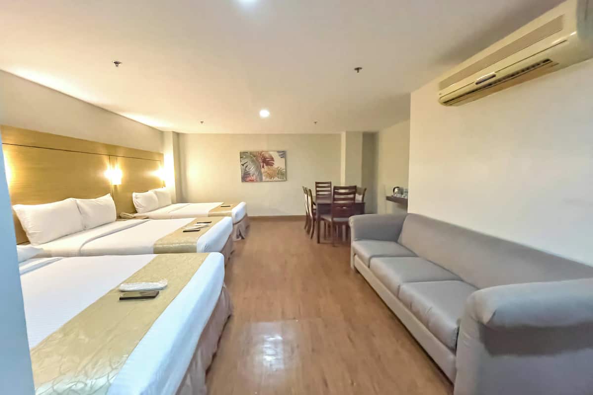 A hotel room with two beds, a sofa, a dining table with chairs, and an air conditioning unit.