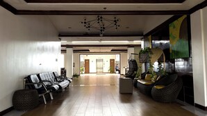 Een ruime lobby met een moderne kroonluchter, lederen zitplaatsen en een grote plant.
